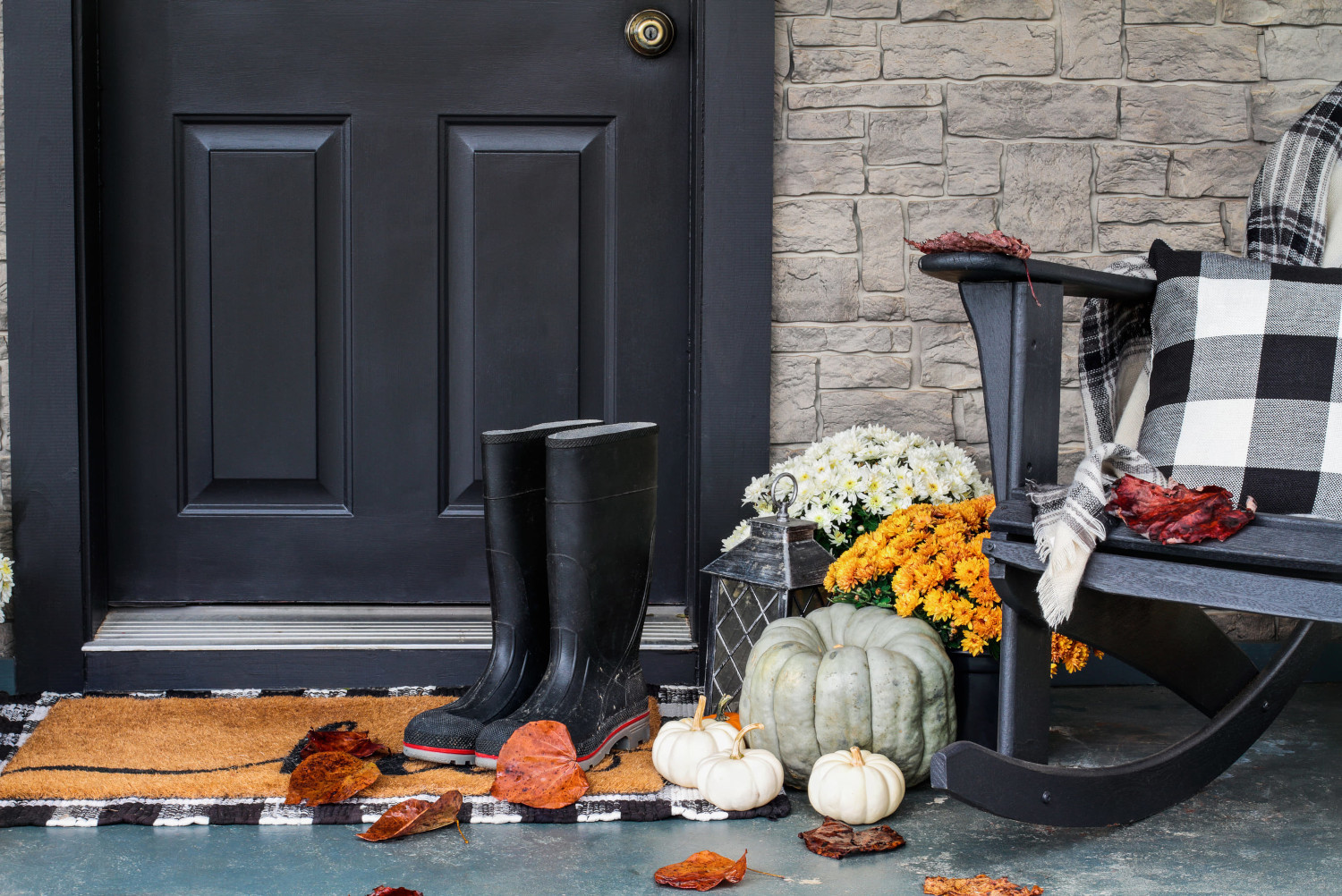 Front porch decorated for fall with pumpkins, mums, plaid pillow and lantern